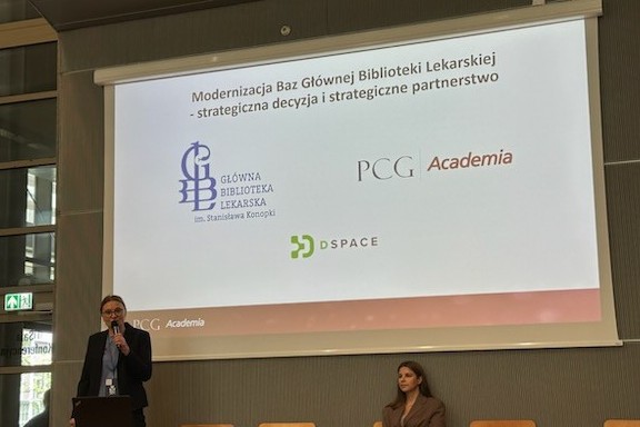 Zdjęcie z konferencji przedstawiające prelegentkę przemawiającą na tle ekranu z napisem „Modernizacja Baz Głównej Biblioteki Lekarskiej – strategiczna decyzja i strategiczne partnerstwo”. Na slajdzie widoczne są logotypy Głównej Biblioteki Lekarskiej, PCG Academia oraz DSpace.